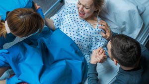 Frau schreit bei der Geburt, Mann und Arzt kümmern sich