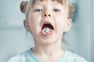 kleines Mädchen mit einer Tablette im Mund